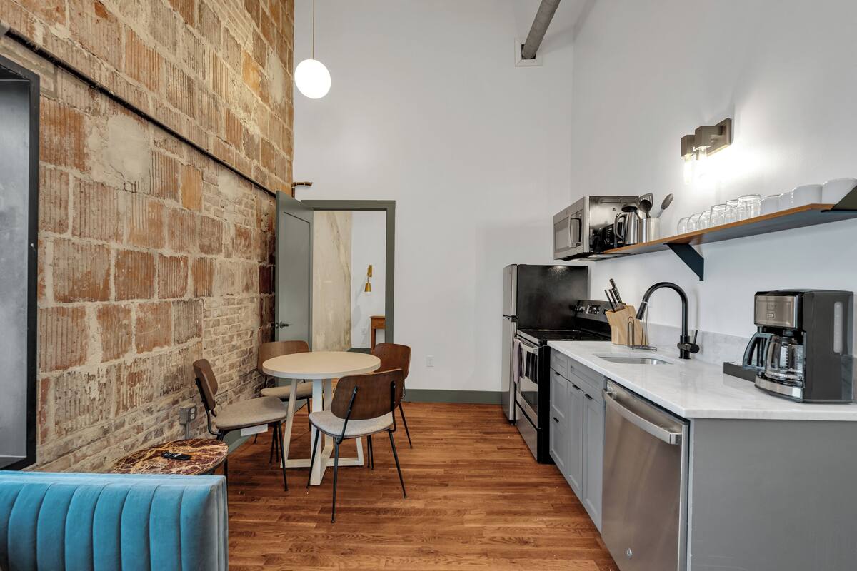 A compact kitchen with a dining area, a brick wall, and a modern light fixture.