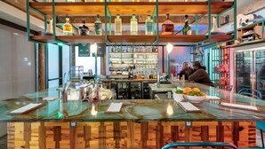 A bar area with a wooden counter, shelves with bottles, and a seating area with chairs. - Schaeffer Hotel (New Orleans)