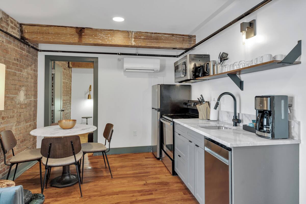 A modern kitchen with a round dining table, chairs, a coffee machine, and a built-in oven.