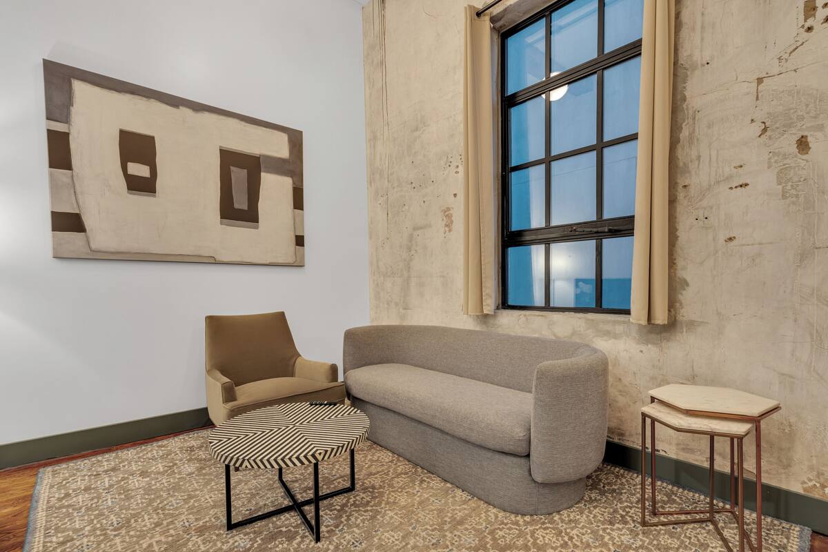 A room with a sofa, a patterned rug, a small table, and a window with a view.