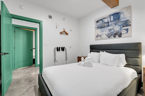 A hotel room with a bed, a green door, a towel rack, a painting, and a wooden headboard. - Schaeffer Hotel (New Orleans)