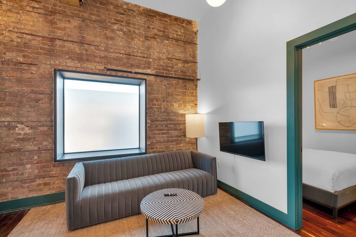 A modern room with a brick wall, a sofa, a round table, a TV, and a bed.