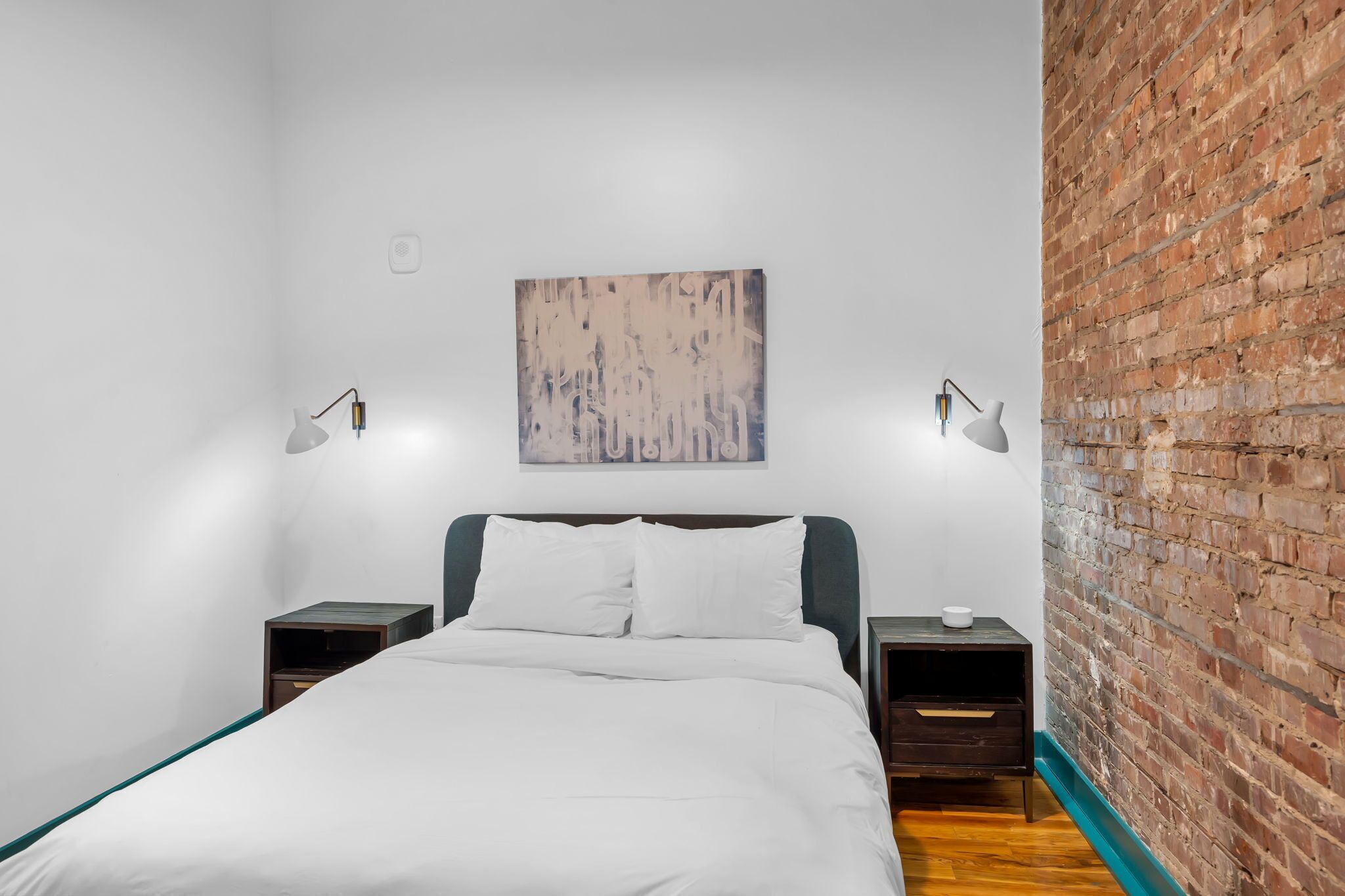 Ein Hotelzimmer mit einem Bett, zwei Nachttischen, einem Wandbild und einer Ziegelwand.