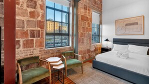 A room with a brick wall, large windows, a bed, a desk, and a chair. - Schaeffer Hotel (New Orleans)