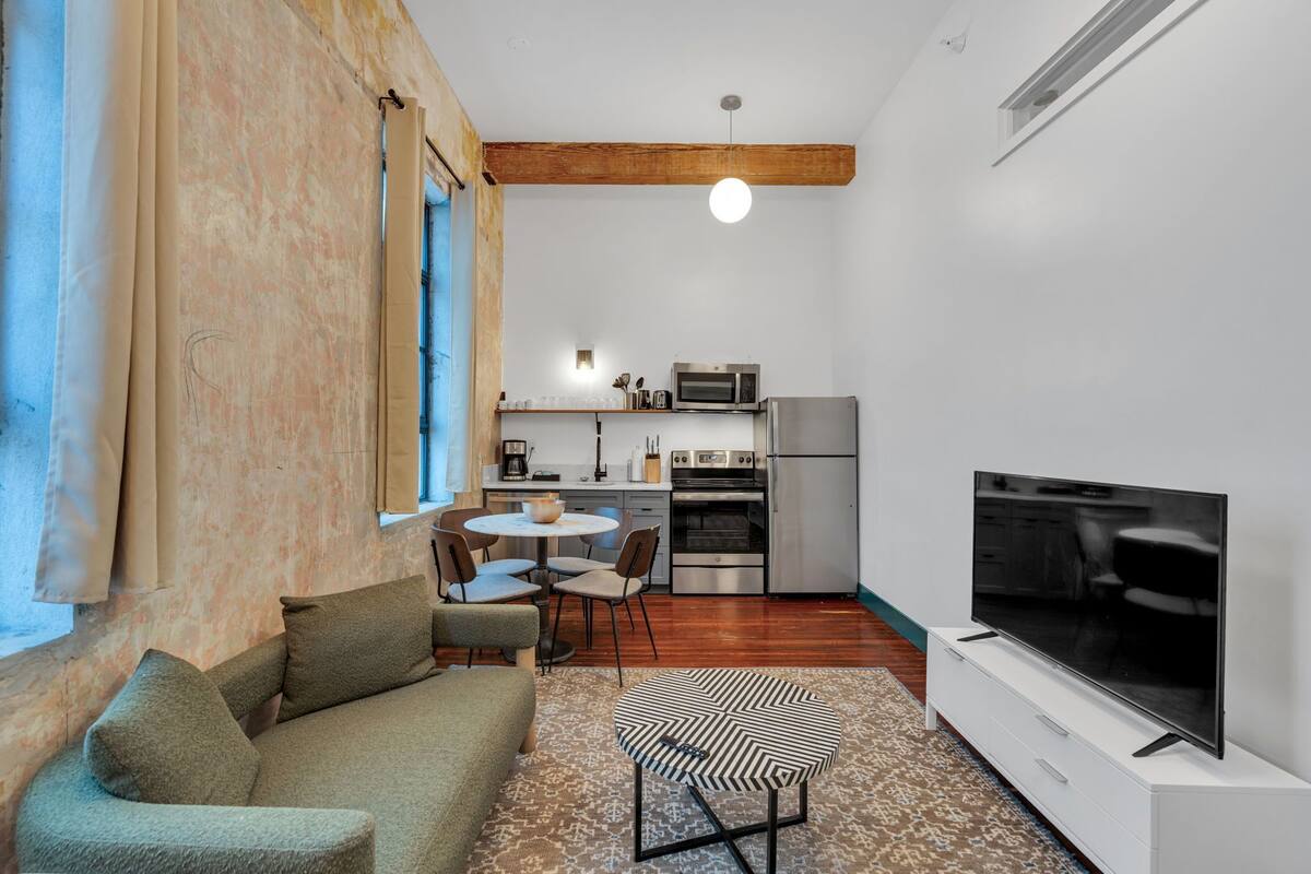 A compact living space with a sofa, a dining table with chairs, a TV, a kitchen area with a microwave, oven, and refrigerator.