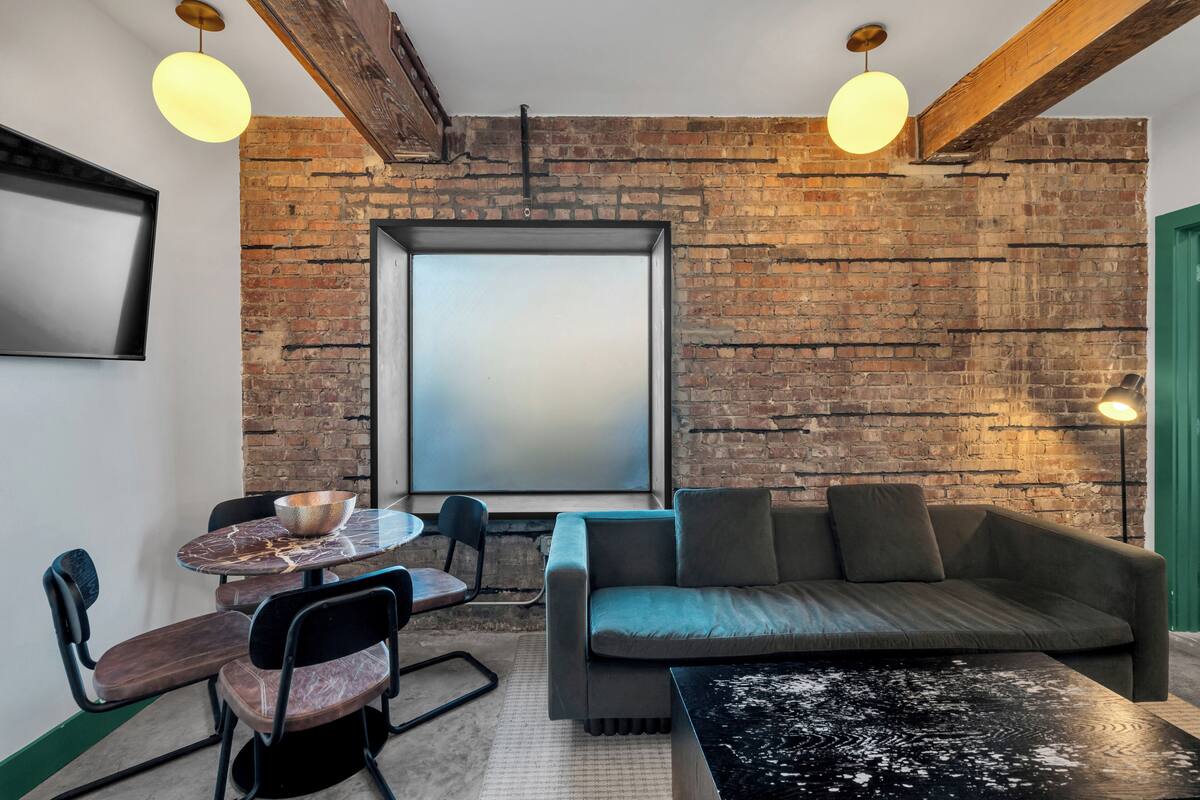 A modern living room with exposed brick walls, a sofa, a coffee table, a dining table with chairs, and pendant lighting.