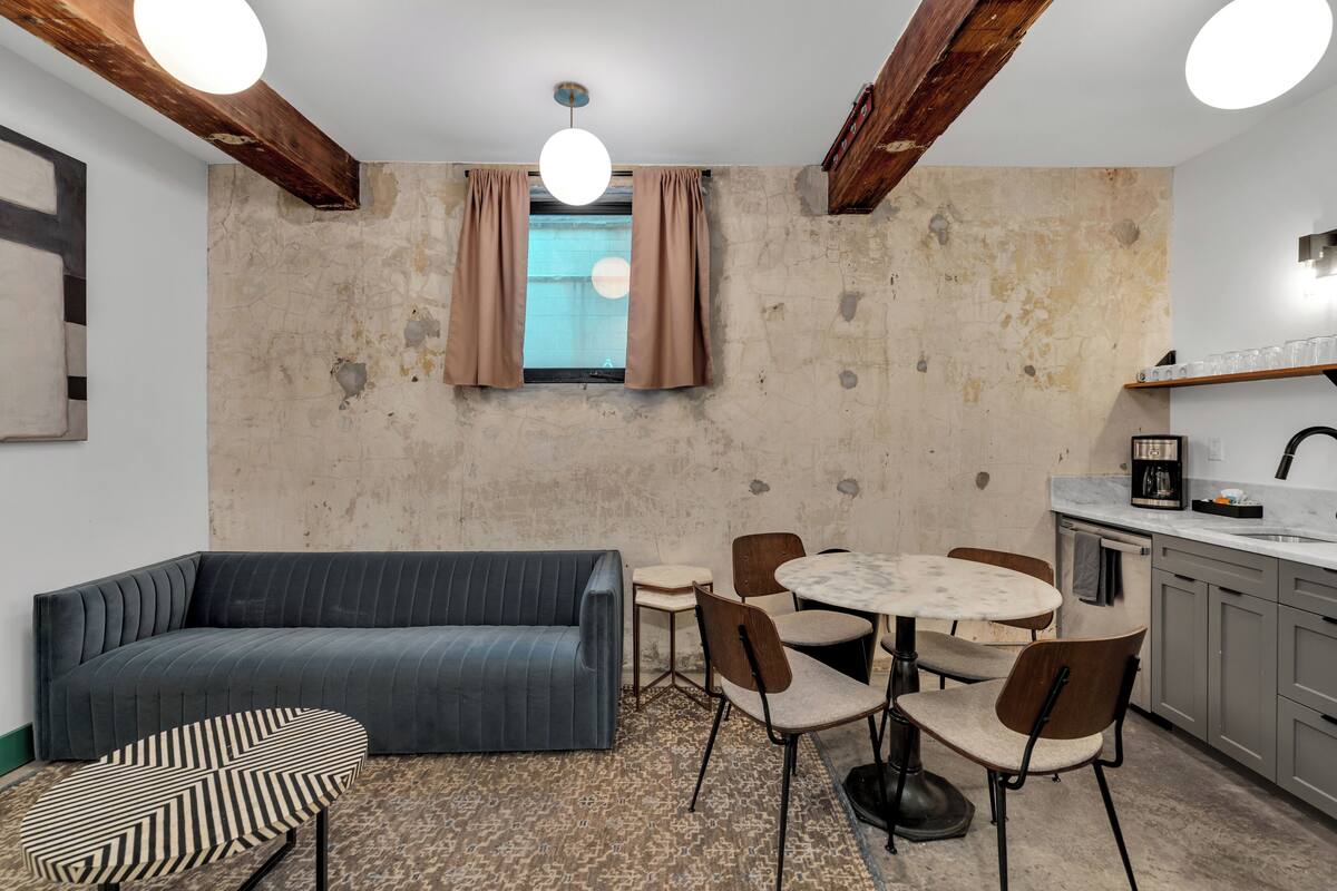 A modern kitchen with a dining area, a sofa, and a patterned ottoman.