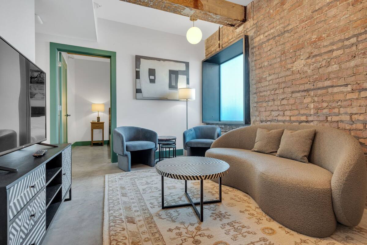 A modern living room with a sofa, two armchairs, a coffee table, a TV, and a lamp.