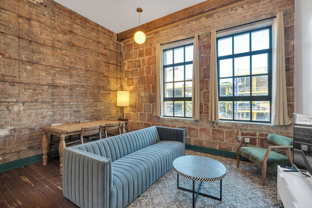 A room with a brick wall, a sofa, a dining table, and a TV.