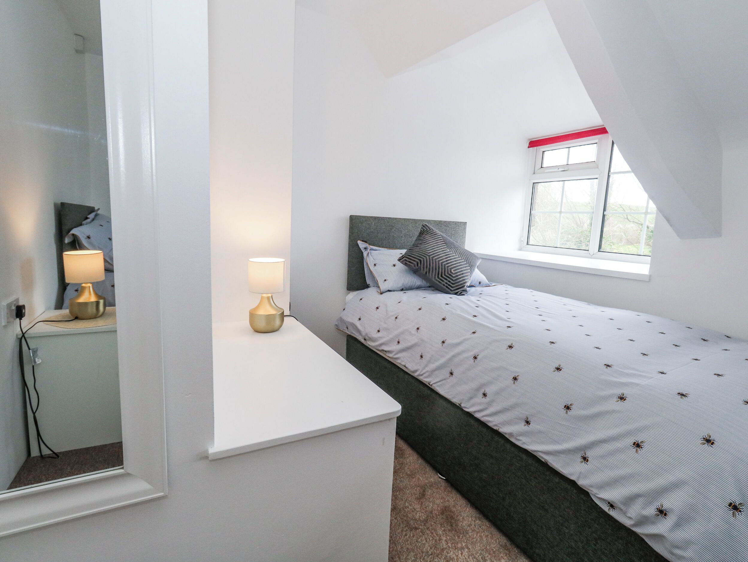 Une chambre à coucher avec un lit, une table de chevet avec une lampe, une fenêtre et un miroir.