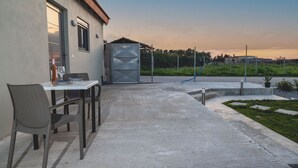Un espace extérieur aménagé avec une table et des chaises, un jardin clôturé et un bâtiment doté d’une porte et de fenêtres.
