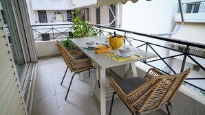 Ein Balkon mit Esstisch für Zwei, Korbstühle, einer gelben Schüssel und einem Blumentopf.