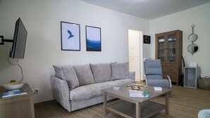 Un salon avec un canapé gris, une table basse, un téléviseur et un meuble.
