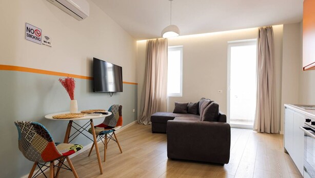 Een moderne woonkamer met een bank, een televisie, een eettafel met stoelen en een keukenhoek.