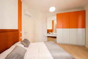 A bedroom with a bed, an orange wardrobe, a white door, and a mirror reflecting a bathroom.