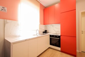 A kitchen with white cabinets, a black oven, and a red refrigerator. - Heart of Durres Apartment 02 (Durrës)