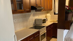 A kitchen with wooden cabinets, a microwave, a stove, and a refrigerator. - Cozy Home in Cholargos (Cholargos)
