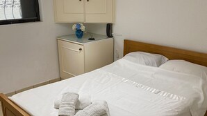 A neatly made bed with white linens and two towels, a bedside table with a vase, and a window with a curtain. - Cozy Home in Cholargos (Cholargos)