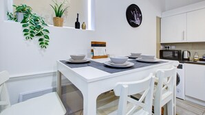 A white dining table with plates and bowls, white chairs, a small potted plant, a framed picture, and a microwave in a kitchen area. - Modern 2BR Apartment 02 with Parking in Greenwich (London)