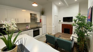 A modern kitchen with white cabinets, a dining area with teal chairs, and a fireplace. - Modern 2BR Apartment 02 with Parking in Greenwich (London)