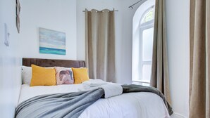 A bedroom with a bed, curtains, a window, and a painting on the wall. - Modern 2BR Apartment 02 with Parking in Greenwich (London)