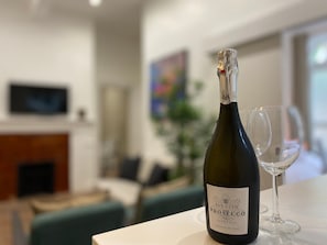 A bottle of San Vito Prosecco on a table with a glass, in a room with a fireplace and a television. - Modern 2BR Apartment 02 with Parking in Greenwich (London)