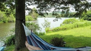 Un hamac est attaché à un arbre au bord d’un lac, et un panneau indicateur se trouve à proximité.