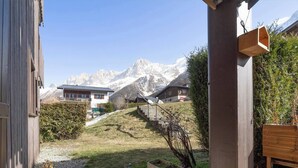 A wooden building with a view of snow-capped mountains, a gravel path, and a wooden bench. - Sunny - Cosy 1CH | 27m2 | Terrasse | 2km Remontées (Les Houches)