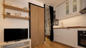 A modern kitchen with white cabinets, a wooden floor, and a TV on a stand. - Sunny - Cosy 1CH | 27m2 | Terrasse | 2km Remontées (Les Houches)