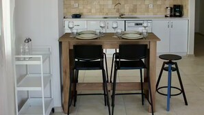 A modern kitchen with white cabinets, a microwave, and a coffee maker. There is a dining table with chairs and a small stool. - Lacivert Apart - Modern House with 180 Degree Unique Kaş View (Gazi)
