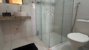 Une salle de bain dotée d’une douche à parois de verre, de toilettes, d’un lavabo avec un plan de travail en marbre et d’un tapis noir sur le sol.