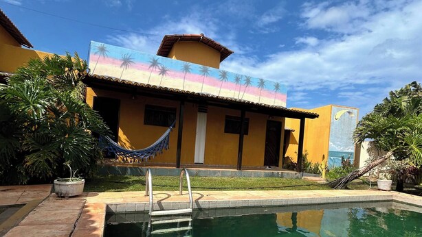 Une piscine avec un escalier, un hamac et un bâtiment orné d’une fresque murale.