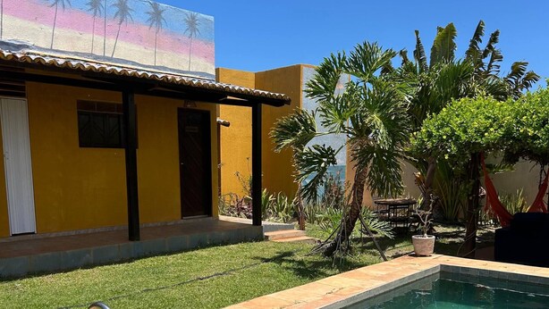 Una piscina con un flotador con la bandera de Brasil, un edificio amarillo con un mural y plantas tropicales.