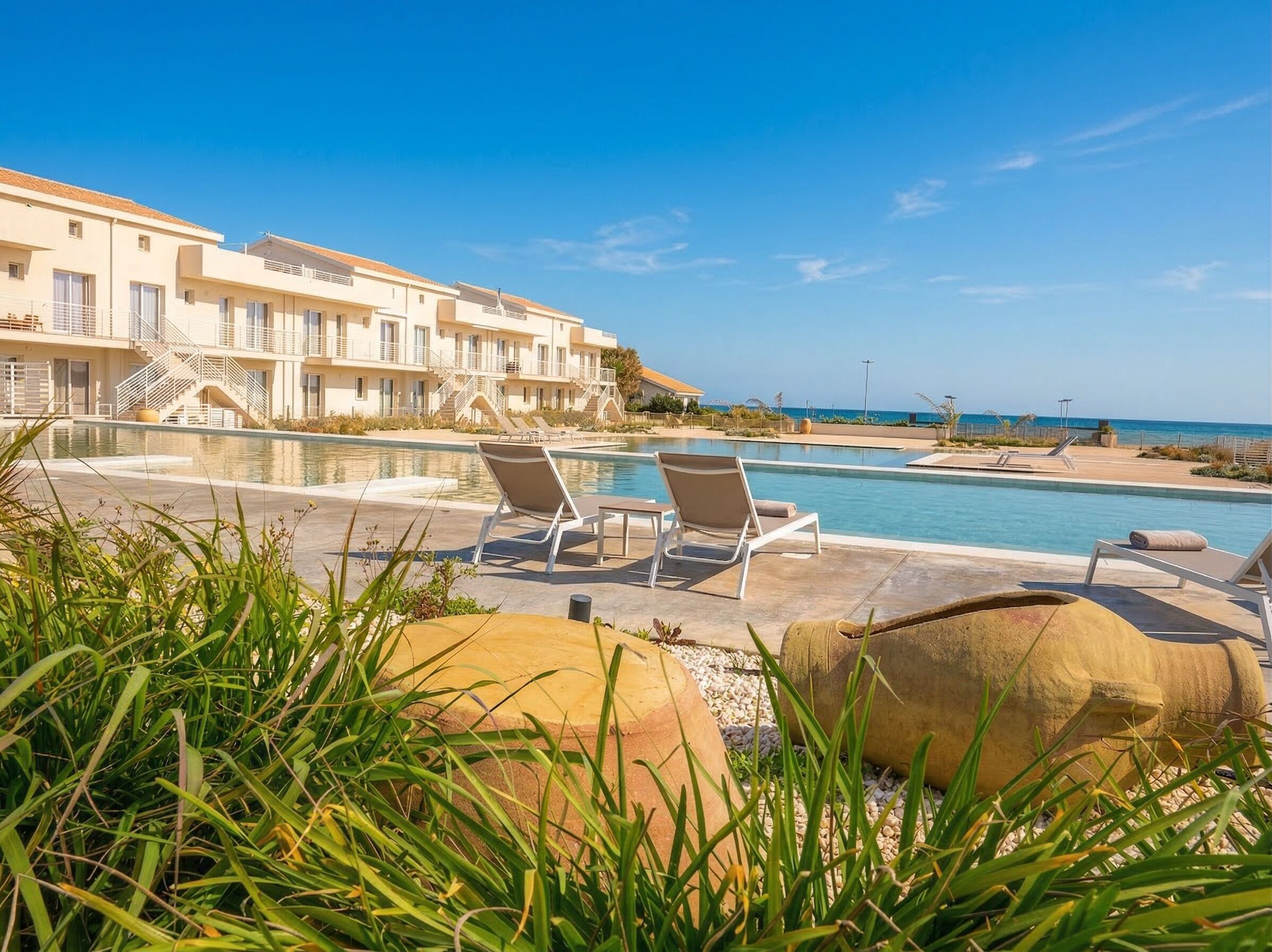 Un espace piscine avec des chaises longues, un bâtiment doté de balcons et une vue sur la mer.