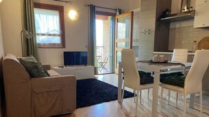 A living room with a sofa, TV, and a dining area with chairs and a table. - Venezia Golf Resort | Terrace & Free Parking (Martellago)