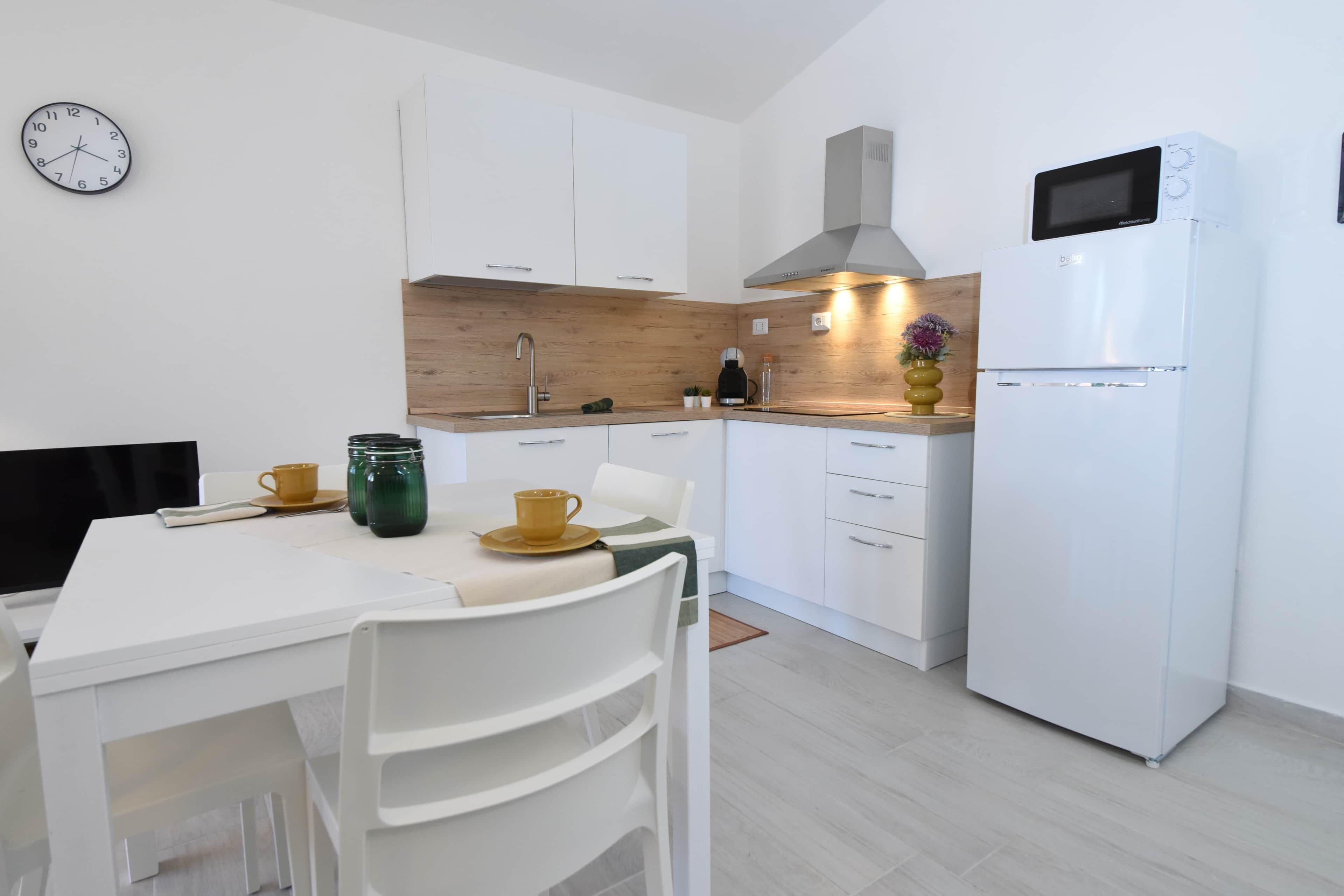 Une cuisine moderne avec des meubles blancs, un four à micro-ondes et une horloge au mur.