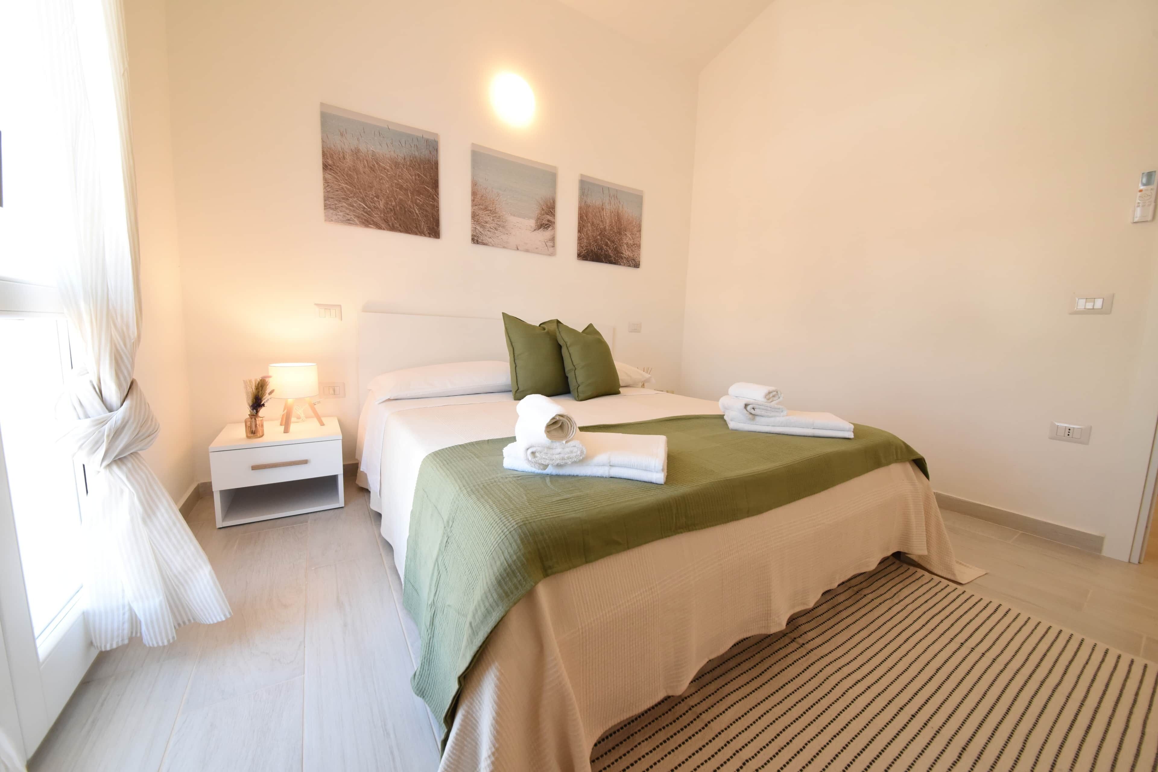 Une chambre d’hôtel comprenant un lit, une table de chevet, une lampe et trois tableaux accrochés au mur.
