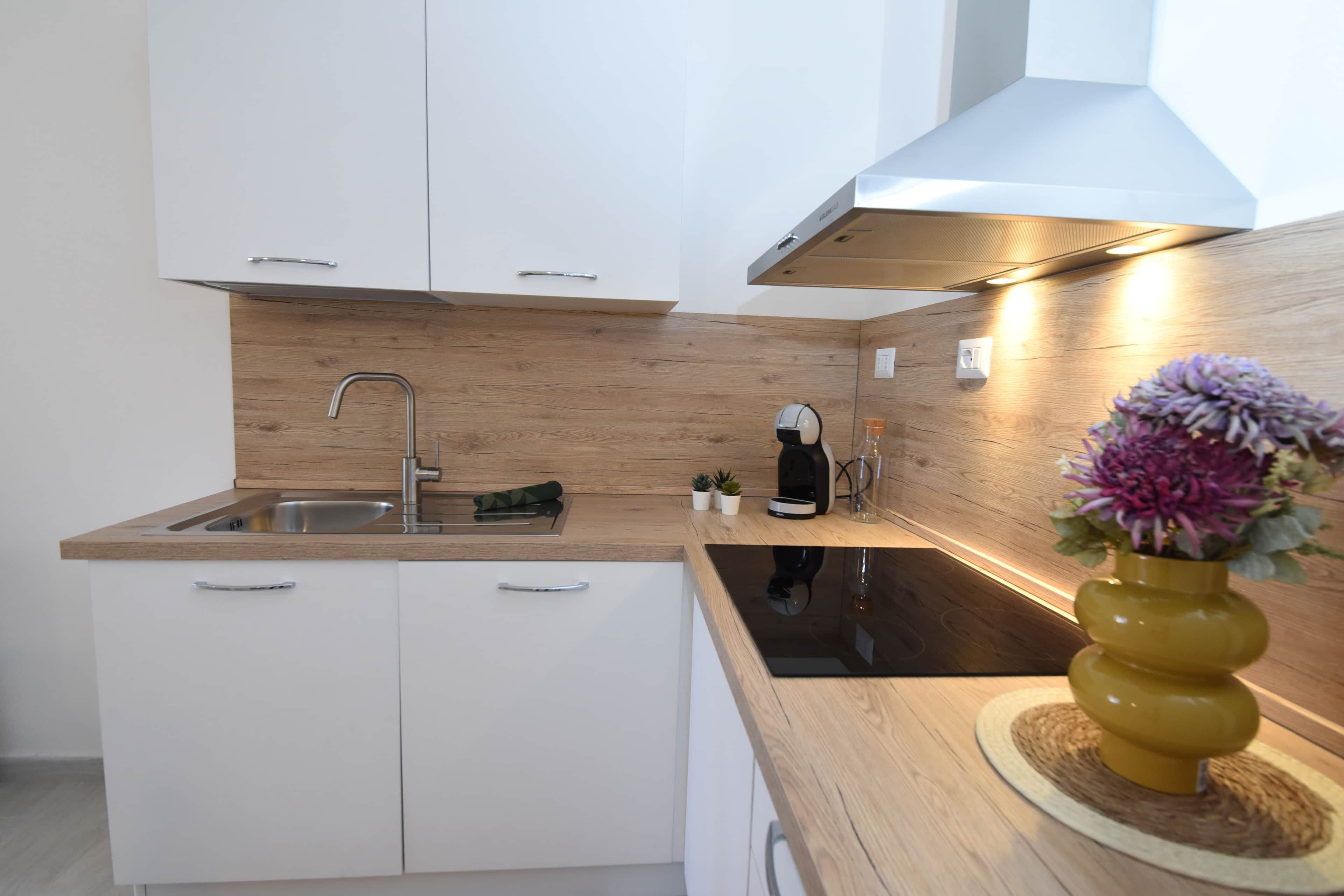 A modern kitchen with white cabinets, a wooden countertop, a stainless steel sink, and a yellow vase with flowers.