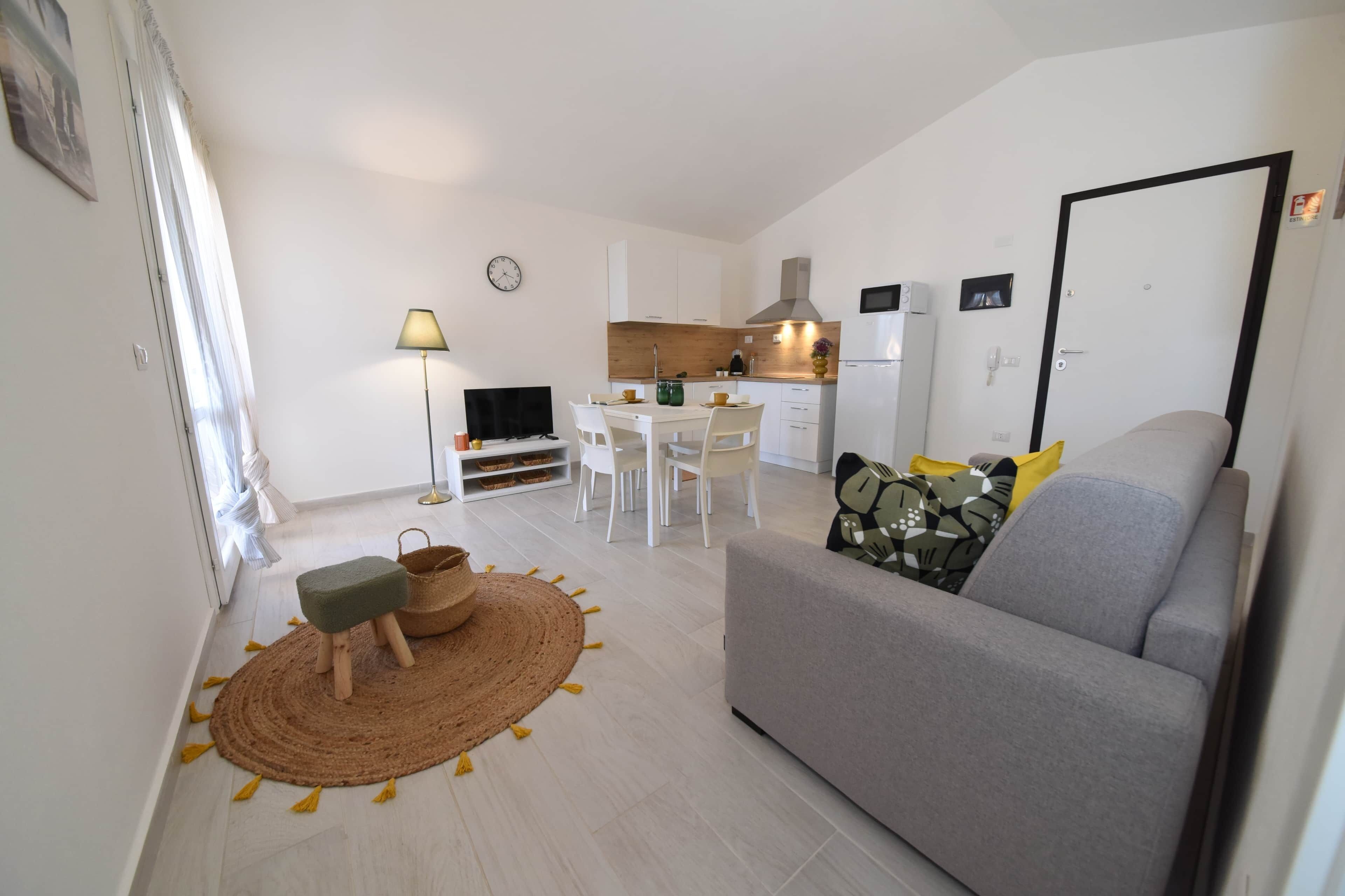 A compact living space with a sofa, a dining table, a kitchen area, and a TV.