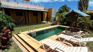 A swimming pool with lounge chairs, a small garden area, and a building with a tiled roof. - Room-nice and Cozy Room With Pool (São Miguel do Gostoso)