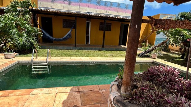 A swimming pool with a ladder, a hammock, and a building with a colorful mural. - Room-nice and Cozy Room With Pool (São Miguel do Gostoso)