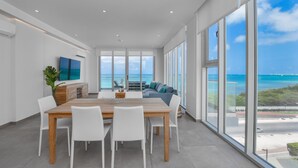 Un intérieur moderne comprenant un coin repas, un canapé et de grandes fenêtres donnant sur l’océan.