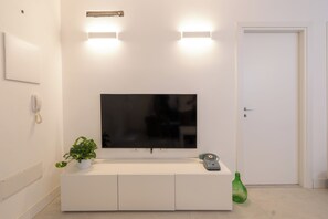A modern living room with a flat-screen TV mounted on a white cabinet, a potted plant, a vintage telephone, and a green bottle on the floor. - Violet House (Cagliari)