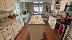 Una cocina con pisos de madera, armarios blancos, encimera de granito y electrodomésticos de acero inoxidable.