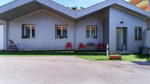 Ein modernes, zweistöckiges Gebäude mit Flachdach, zwei Fenstern, einer Tür und einer kleinen Außenbereich-Sitzgelegenheit mit Stühlen.