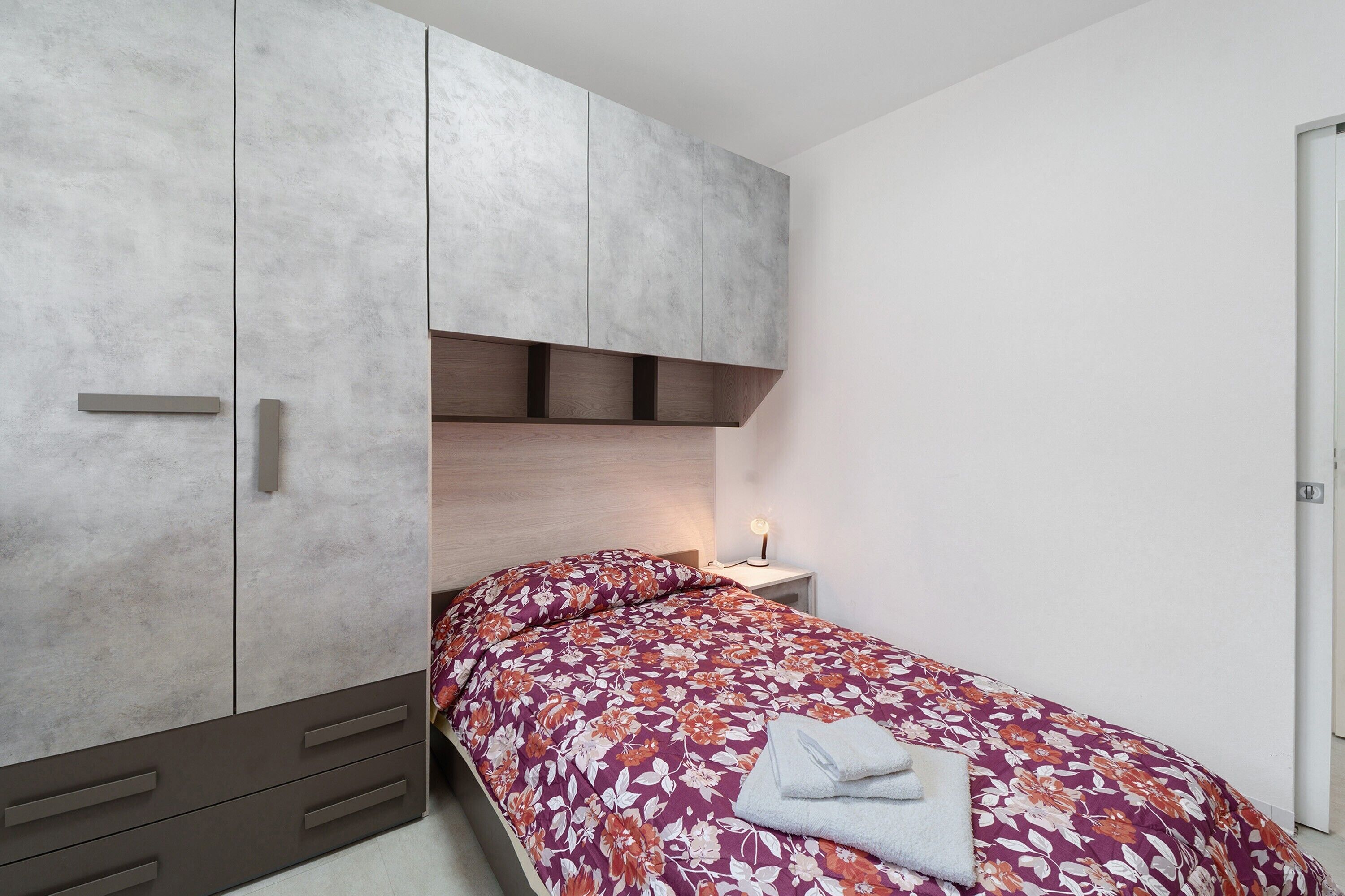 Un dormitorio con cama, armario, mesita de noche y velador.