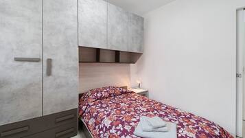 Un dormitorio con cama, armario, mesita de noche y velador.