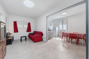 A modern living room with a red sofa, a small table, and a dining area with red chairs. - Casa Cortina – Holiday Apartment in Central Domodossola with Parking and WiFi (Domodossola)