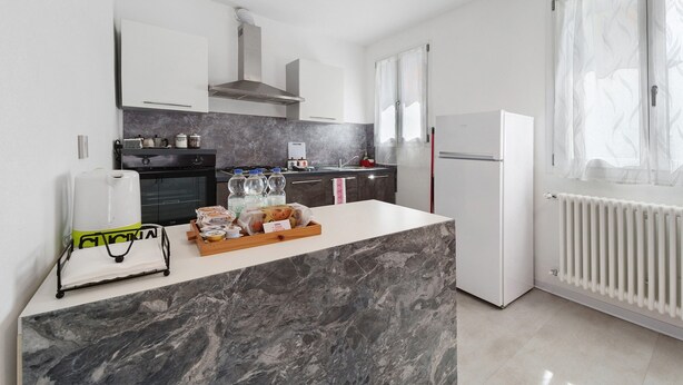 Eine moderne Küche mit Marmorarbeitsplatte, weißen Schränken, einem Einbauofen und einem Kühlschrank.