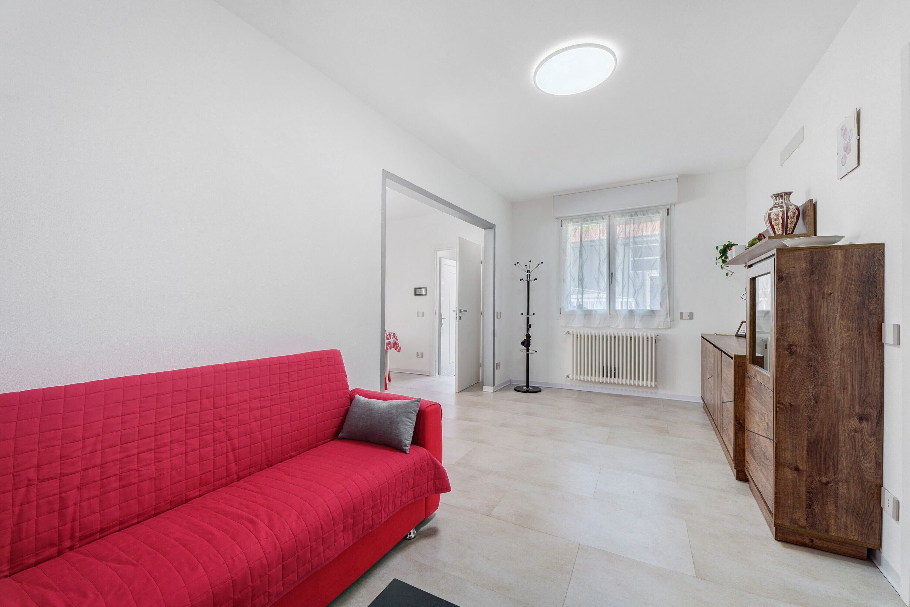 A room with a red sofa, a wooden cabinet, and a radiator.